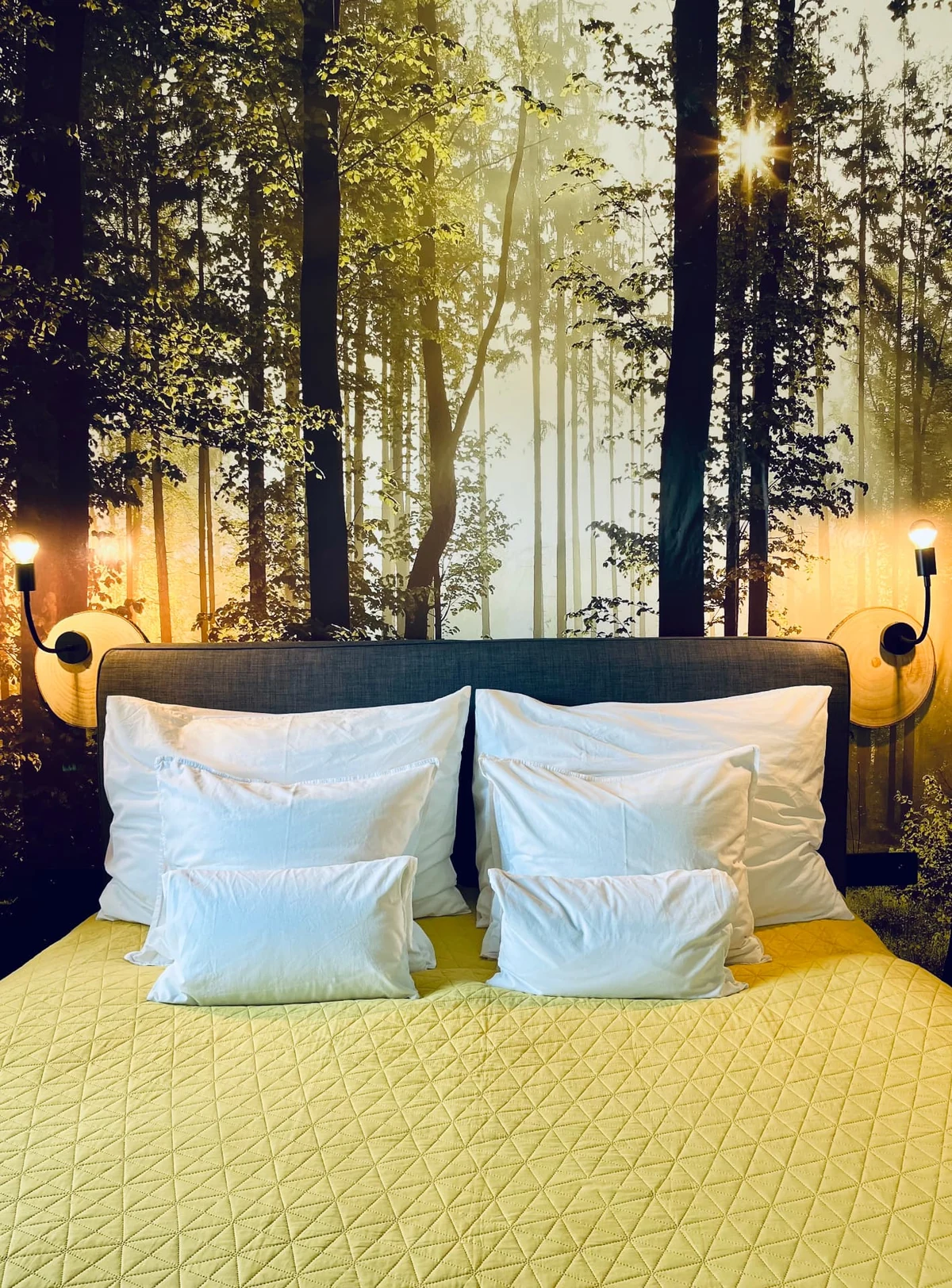 Postel s lesní tapetou a rozsvícenými lampami v apartmánu HYGGE