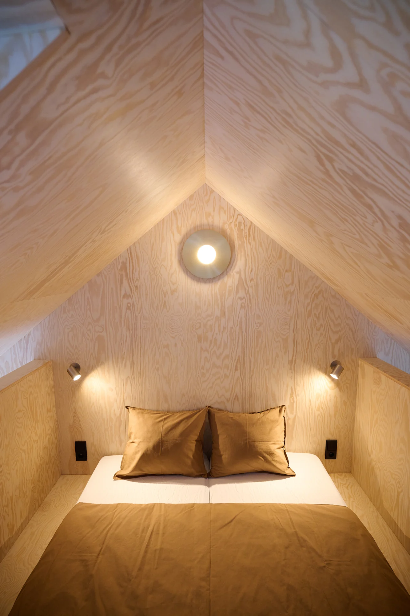 An attic bedroom under the gable, warmly lit, with ochre bedding