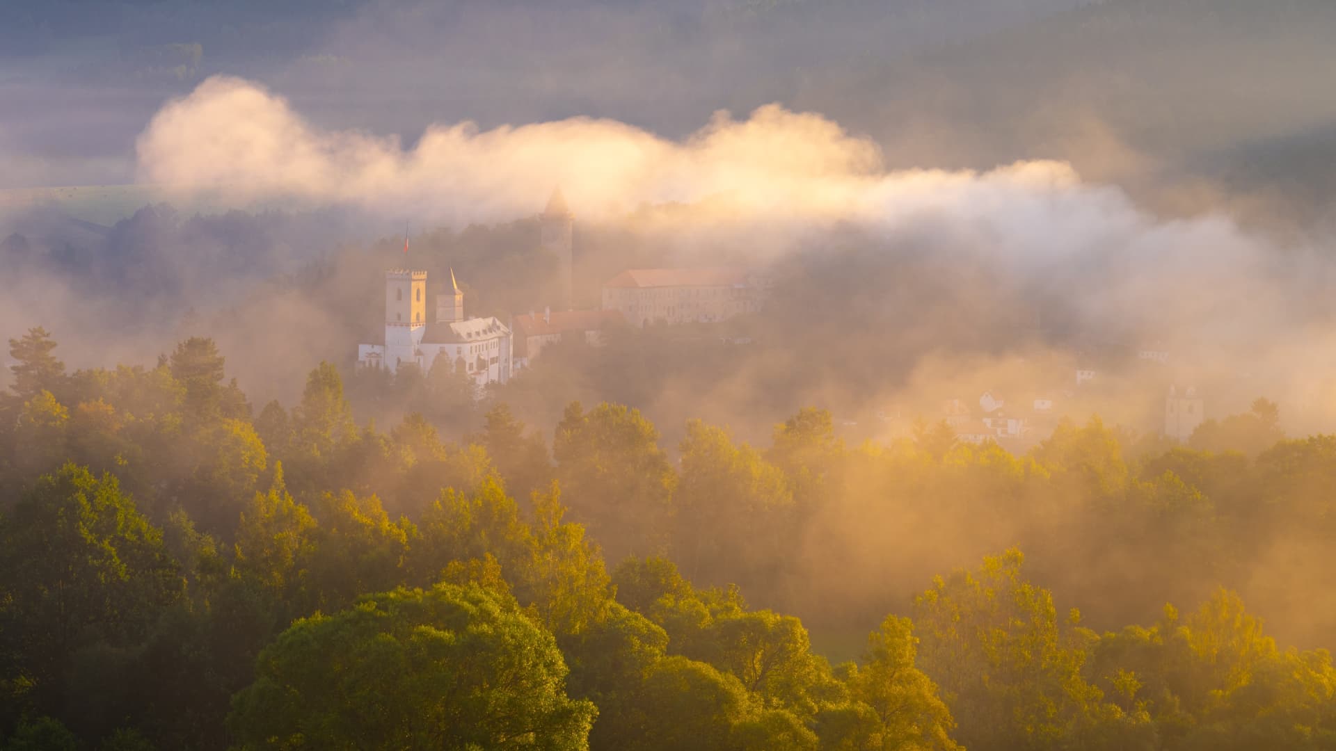 A castle shrouded in morning mist above a forested valley