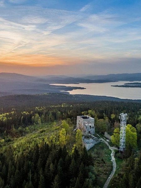 The Vítkův hradek ruin and its tower above the forest and the lake at sunset