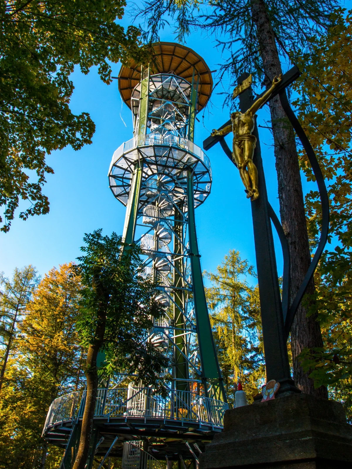 The Dobrá Voda observation tower and a roadside cross among trees in autumn light