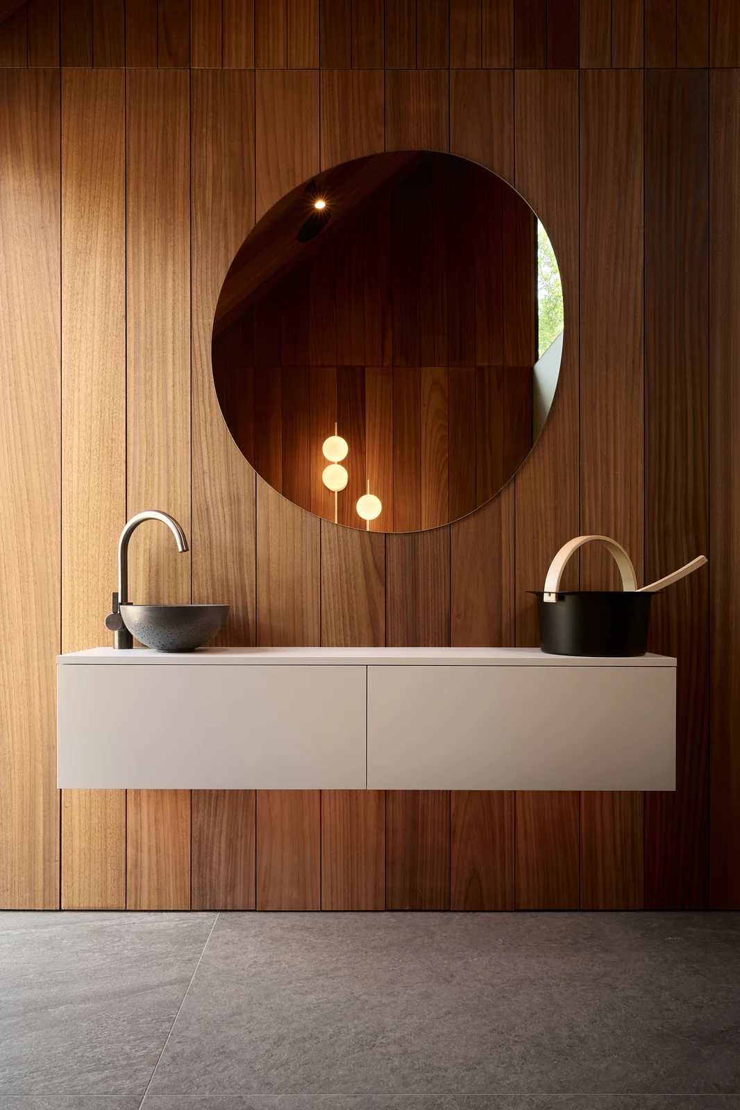 White vanity with a round mirror against a dark wood wall